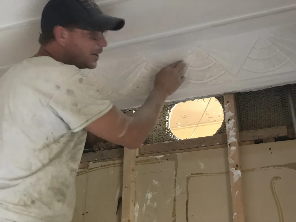 A plasterer repairing decorative fan-shaped ceiling ornament