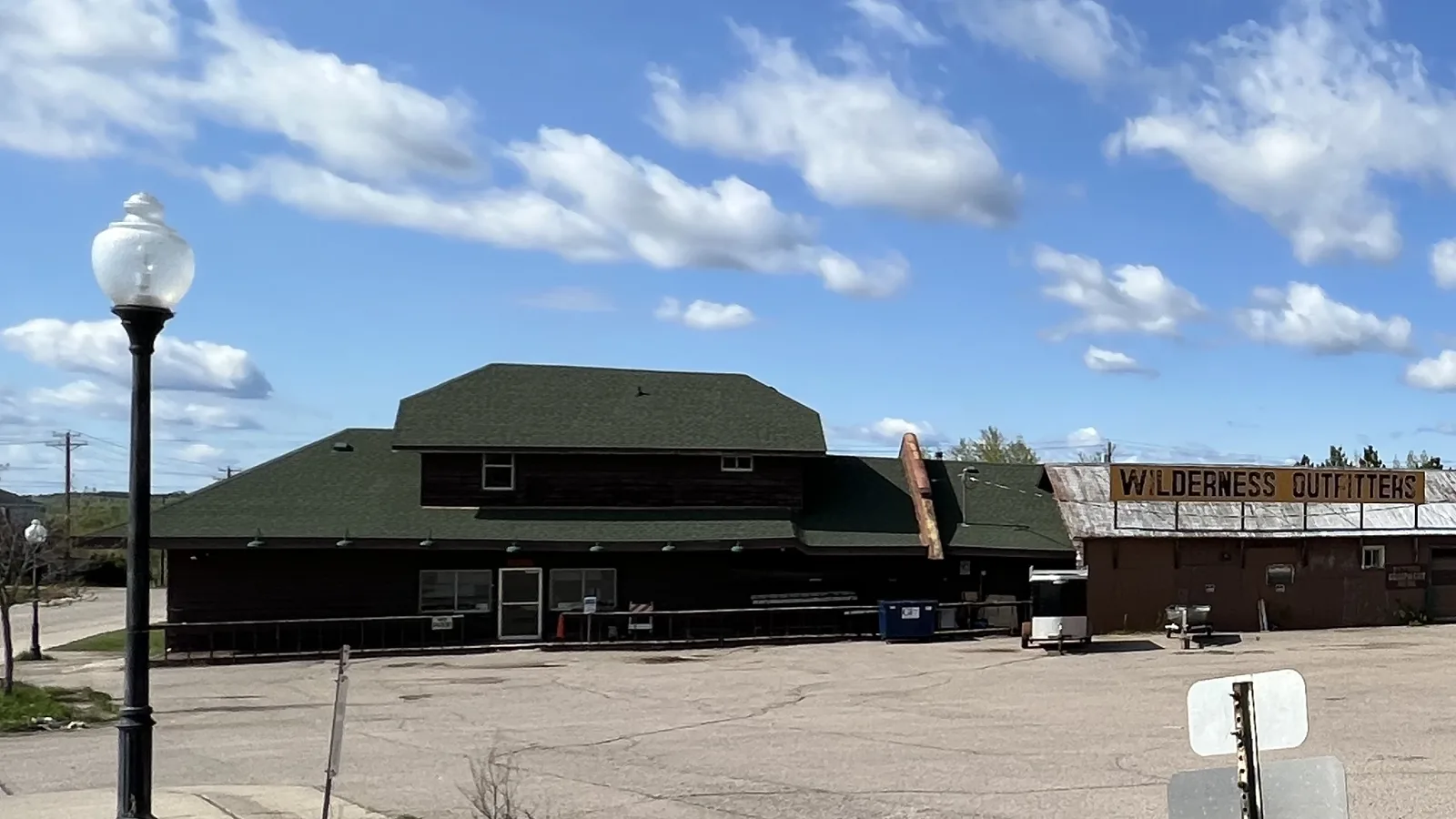 The depot with dark brown siding and a green roof beside a gravel lot before renovation