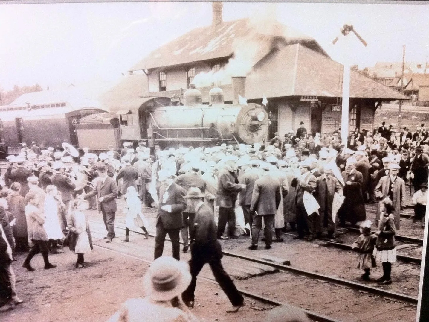A large crowd and a brass band fill the platform as a steam locomotive stands in front of the Ely depot