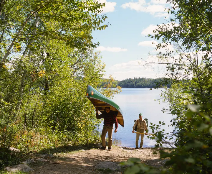 Two men carrying a canoe along a portage trail to a lake