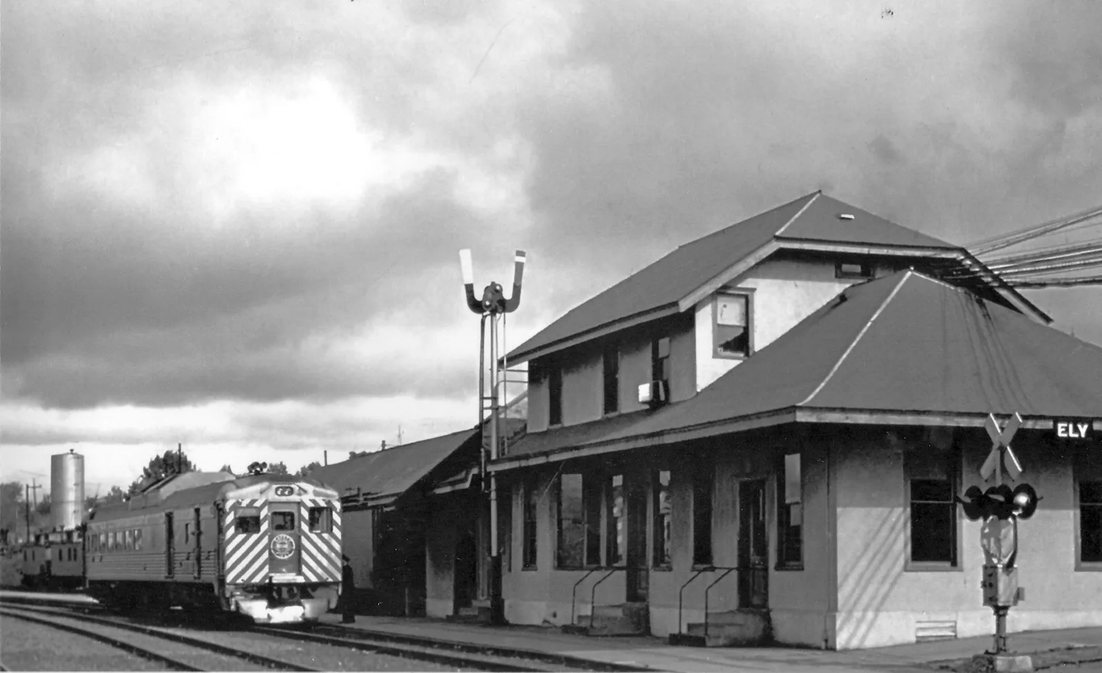 A self-propelled passenger railcar beside the stucco Ely depot