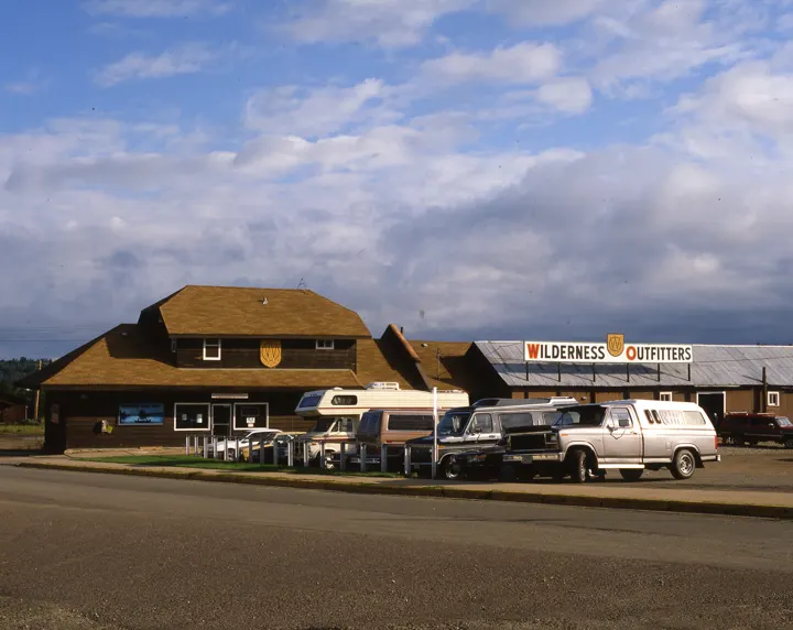The depot with dark brown siding and a Wilderness Outfitters shield, with trucks and campers parked in front