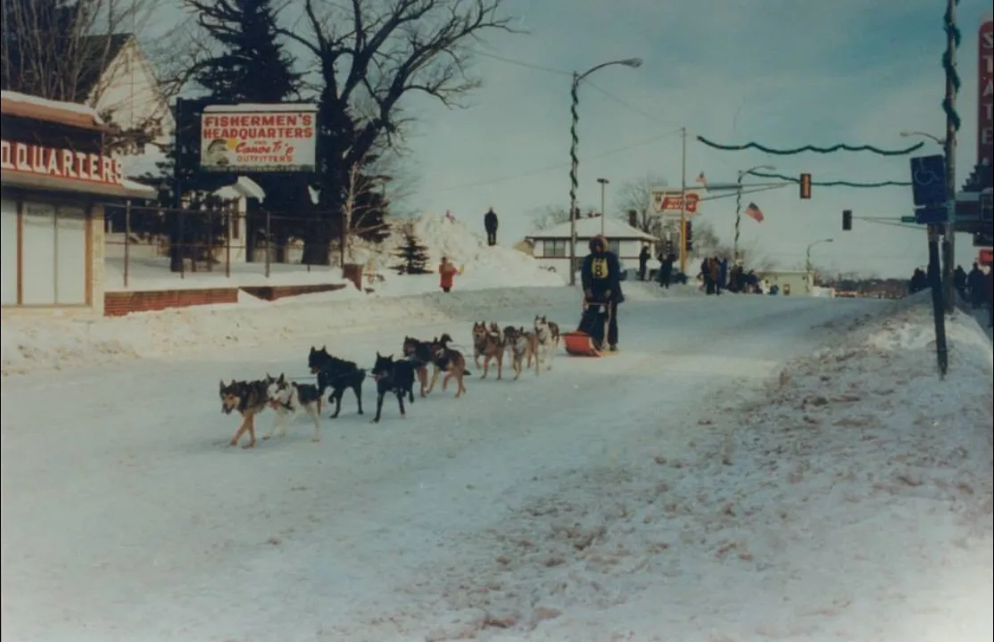 A sled dog team running down a snowy Sheridan Street past the Fishermen's Headquarters sign