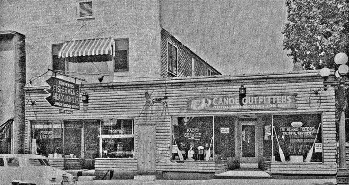 The Fishermen's Headquarters and Canoe Outfitters storefront with a hanging sign, canoe paddles in the windows and signs for fishing licenses, radio service and outboard motors