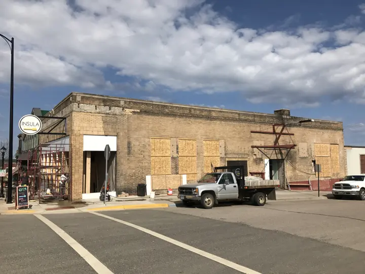 The brick building with boarded windows, scaffolding and an Open, Please Use Side Door sign