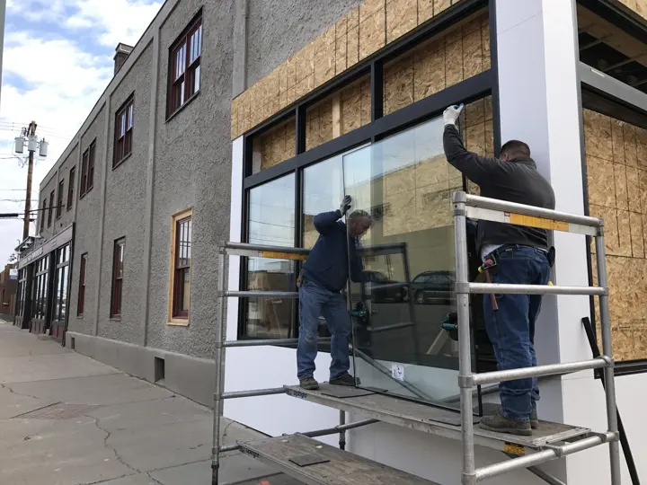 Two glaziers on scaffolding setting a large pane into a new storefront