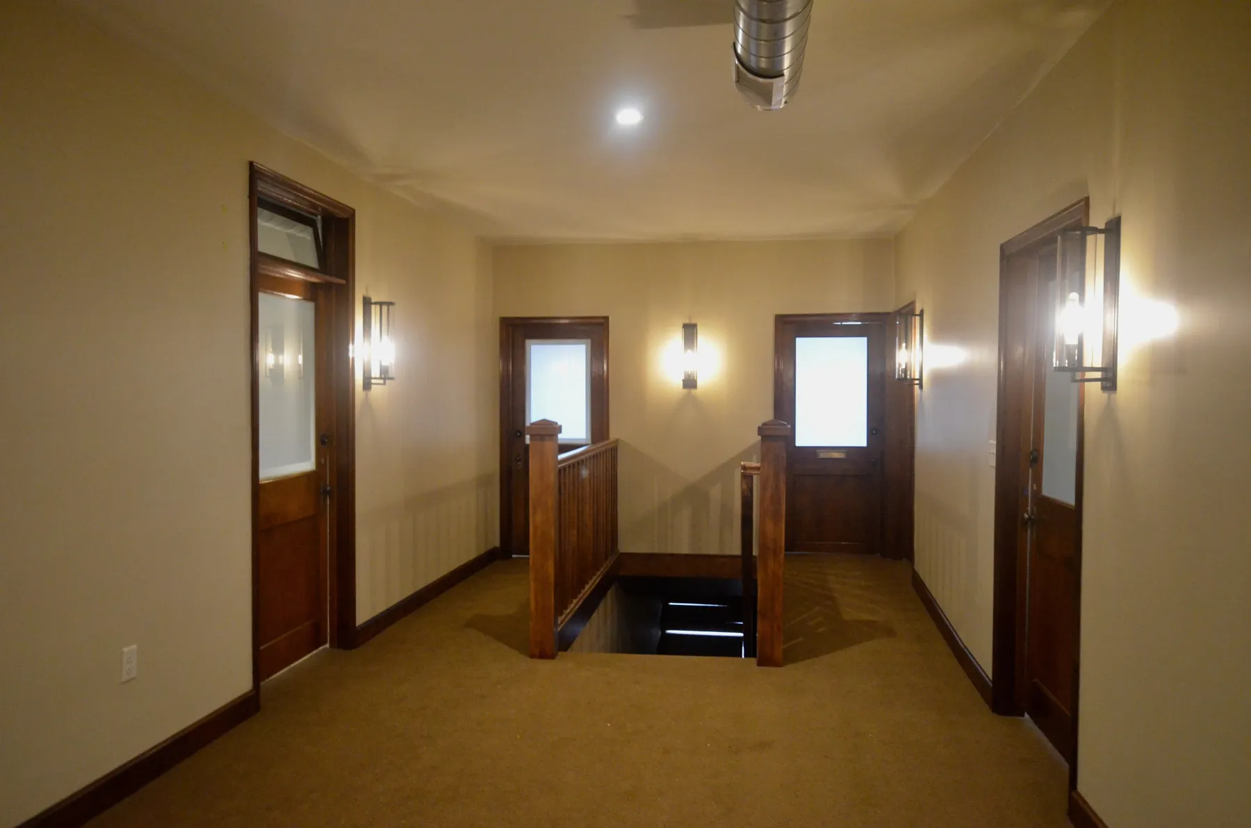 Upstairs hallway with wood office doors and wall sconces