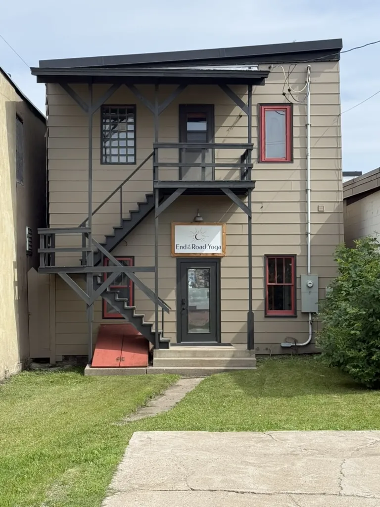 The back of the building with an End of the Road Yoga sign, a covered stair and red-trimmed windows