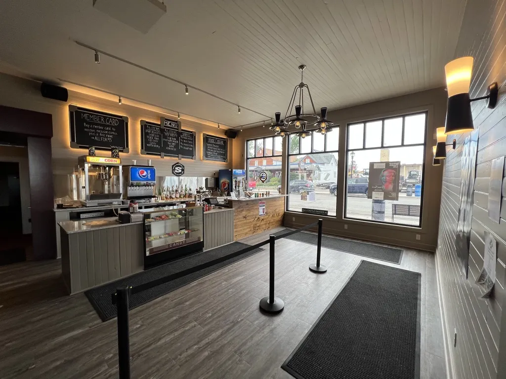 The finished concession lobby with popcorn machine, candy case, chalkboard menus, a chandelier and big windows