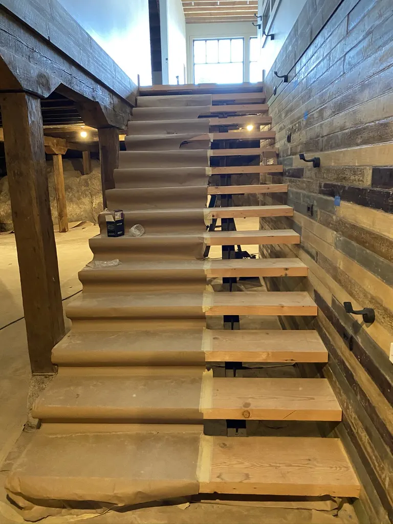 A new open-tread stair beside a reclaimed barnwood wall, still covered in protective paper