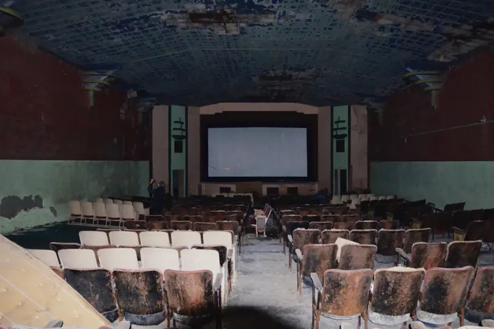 The dark auditorium with rows of worn seats facing the screen, flanked by Art Deco light towers
