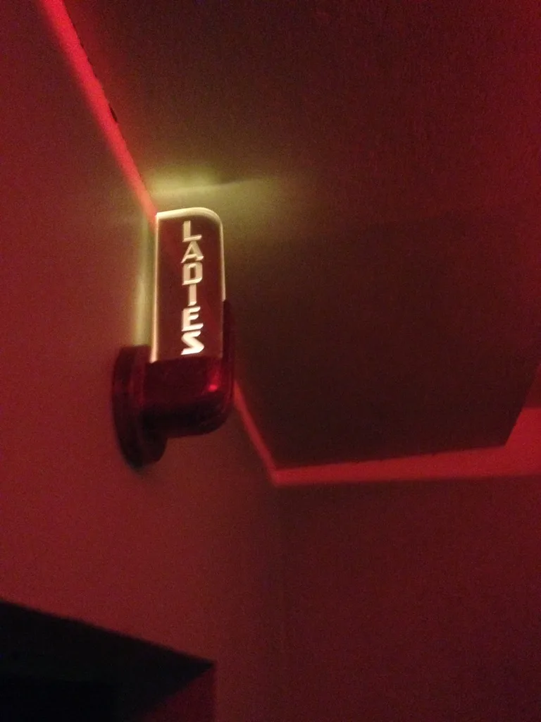 A glowing Art Deco LADIES sign on a red-lit wall