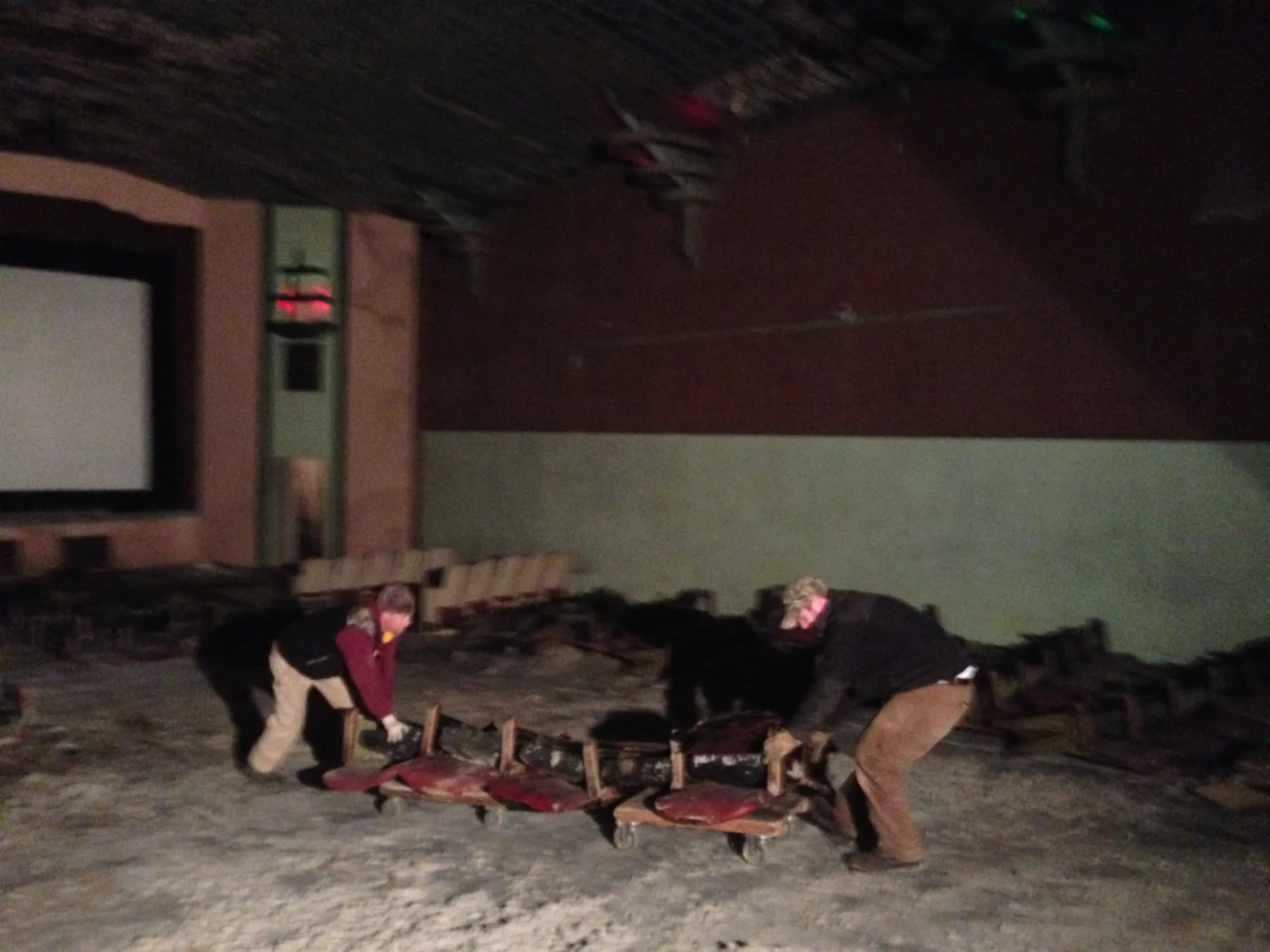 Two workers wheeling a row of old seats out of the auditorium