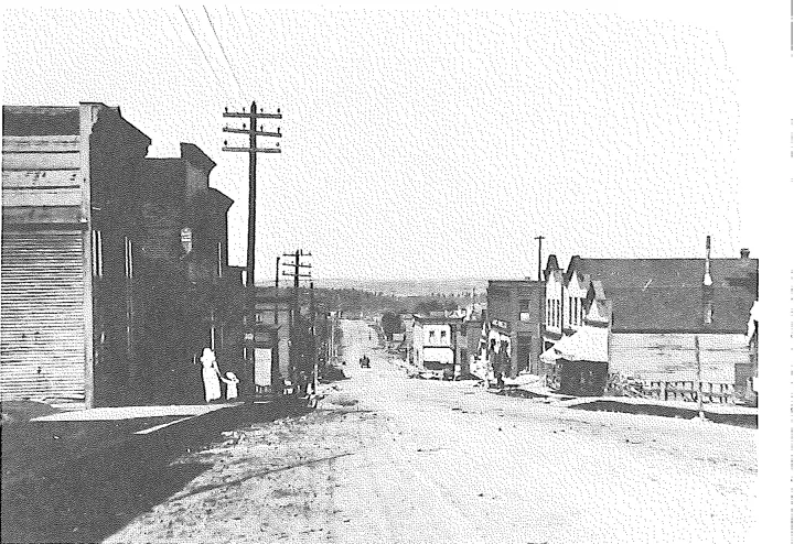 An unpaved Ely street around 1910 lined with wooden storefronts and power poles