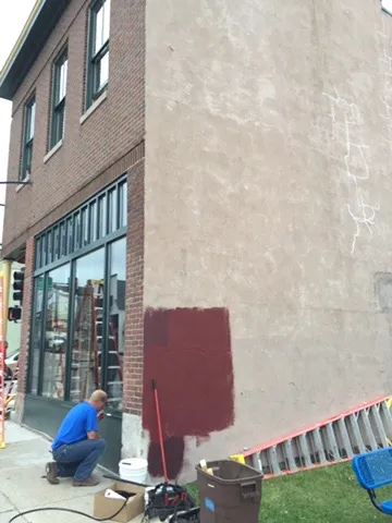A painter testing a red color on the stucco side wall