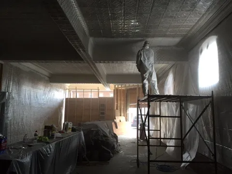 A worker in a protective suit on scaffolding painting the tin ceiling